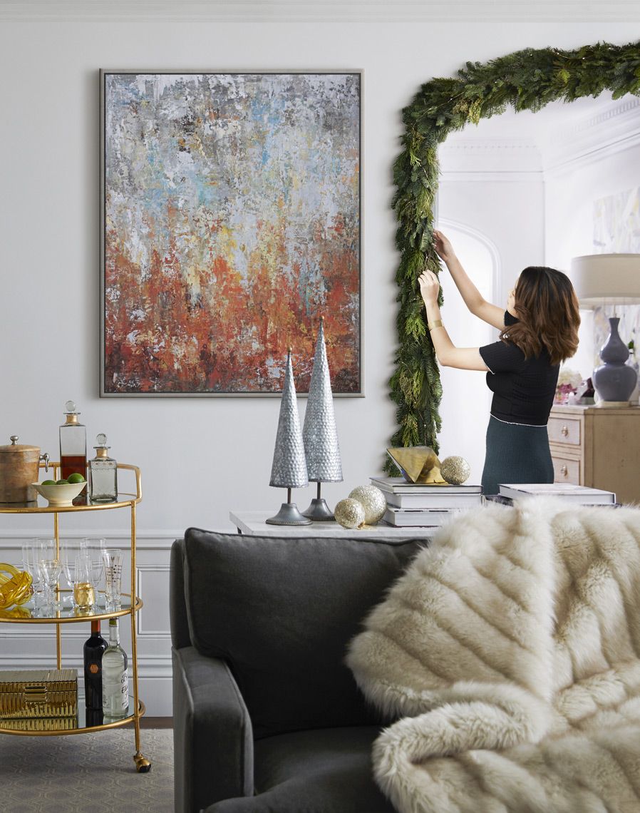 Woman decorating hanging garland in archway for the holidays with painting above bar cart in contemporary house 