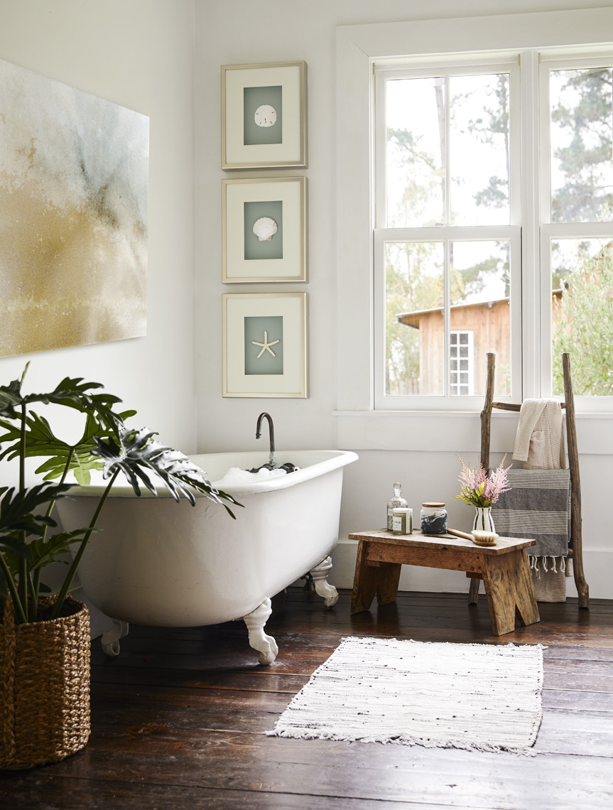 Farmhouse bathroom with framed art on wall potted plants clawfoot tub rustic floor
