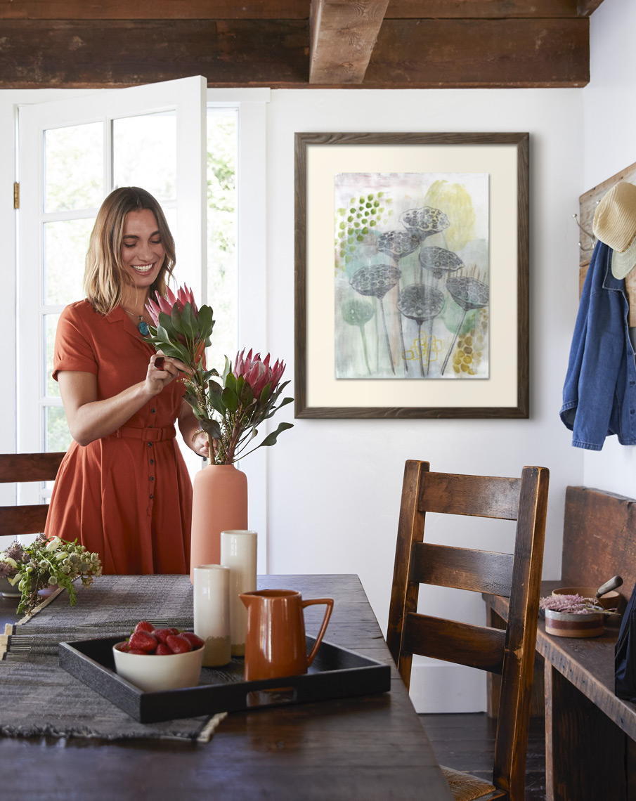 Woman making protea floral arrangement in vase with framed art print on wall in farmhouse dining room Sean Dagen Photography